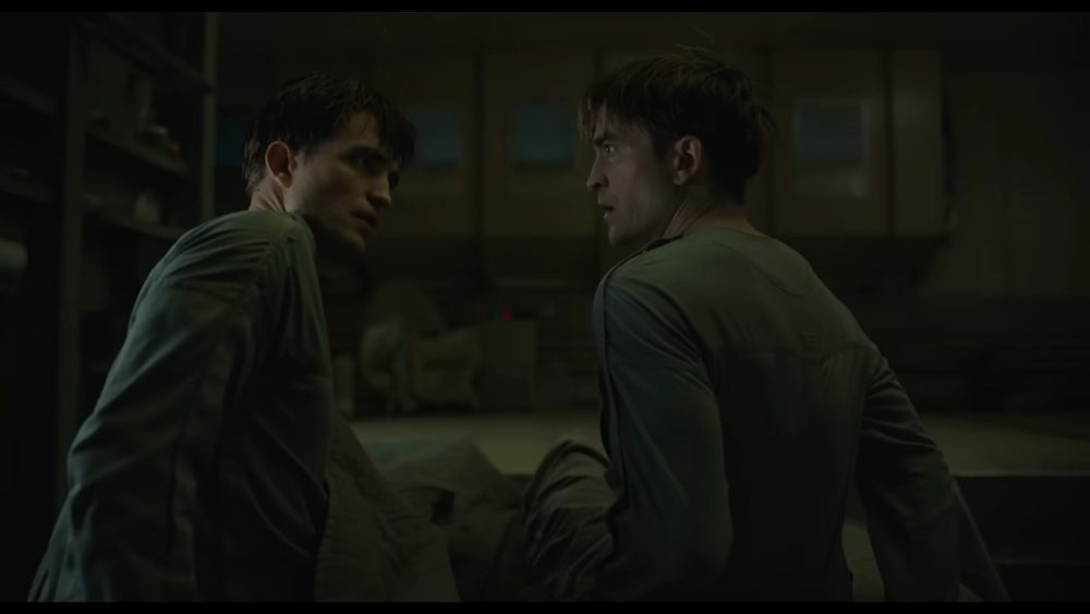 mickey 17. clones of robert pattinson stare at each other while sitting up in bed.
